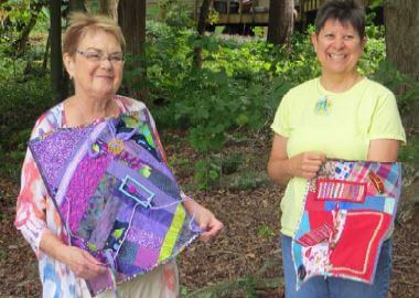 local crafters Andrea Shipley and PJ Howard showing off the "busy quilts" that they made