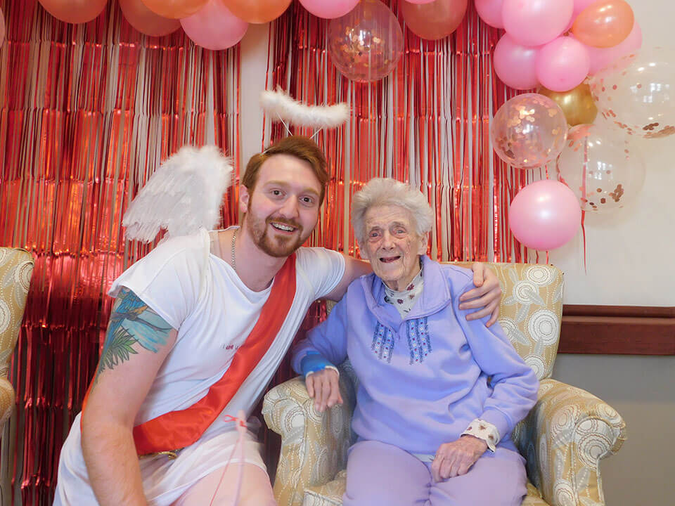 Senior woman posing next to man dressed as cupid with valentine's day decor